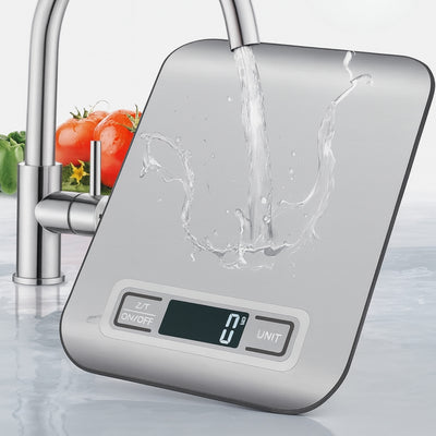 Digital kitchen scale with water splashing on it, vegetables in the background