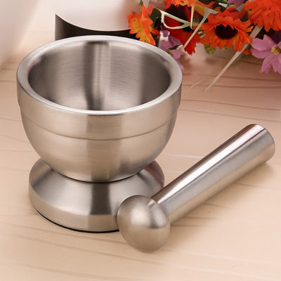 Stainless steel mortar and pestle on a wooden surface with flowers in the background