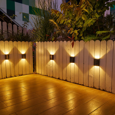 Wooden fence with wall-mounted lights casting a warm glow on a wooden deck.