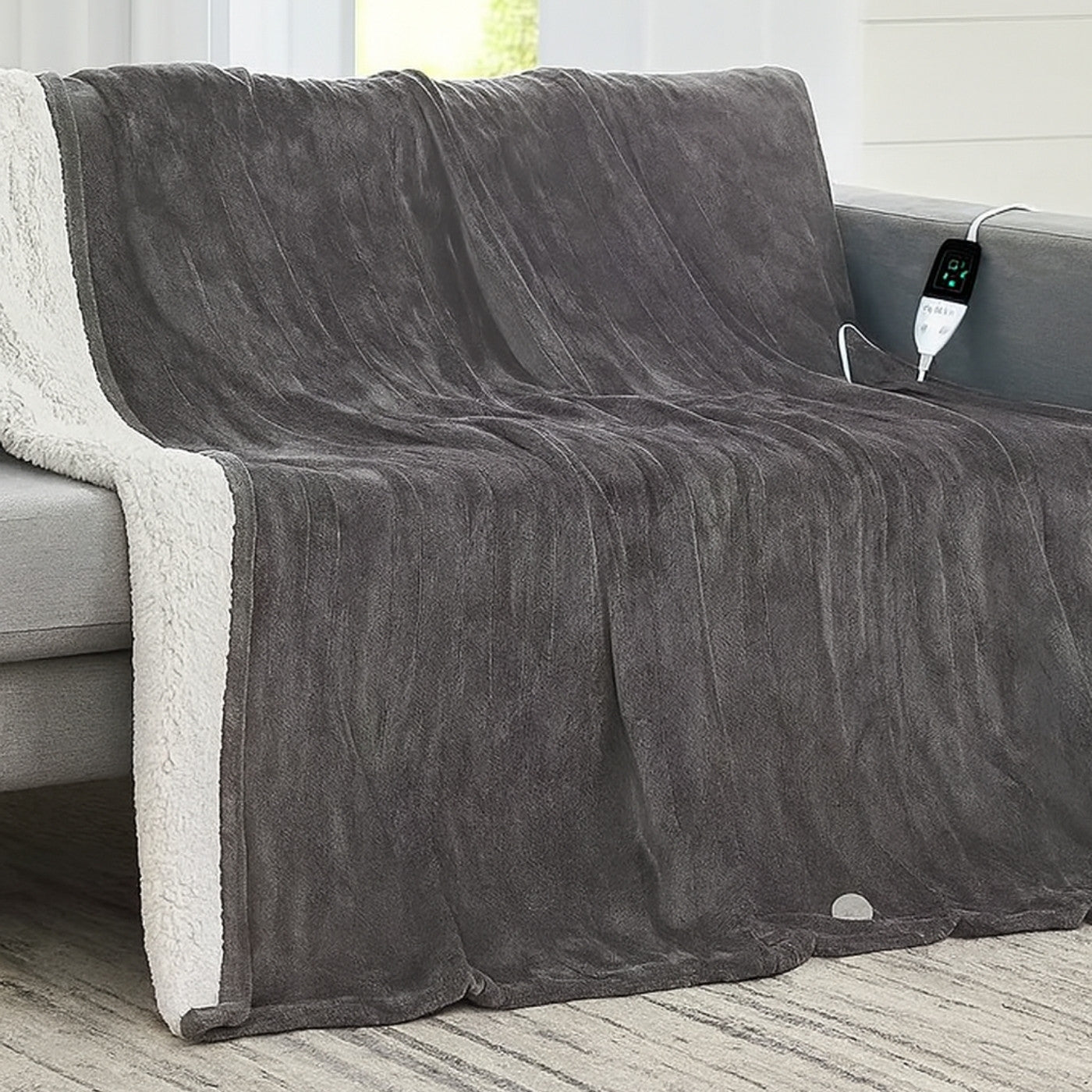Gray electric blanket draped over a sofa with a power cord visible.